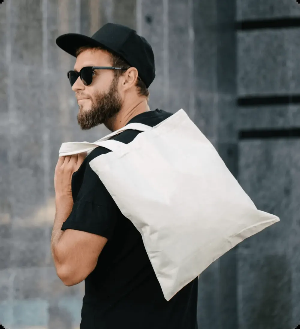 Man wearing a black cap and t-shirt carrying a canvas tote bag